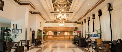 A spacious lobby with a central reception desk, seating areas, and a decorative ceiling.