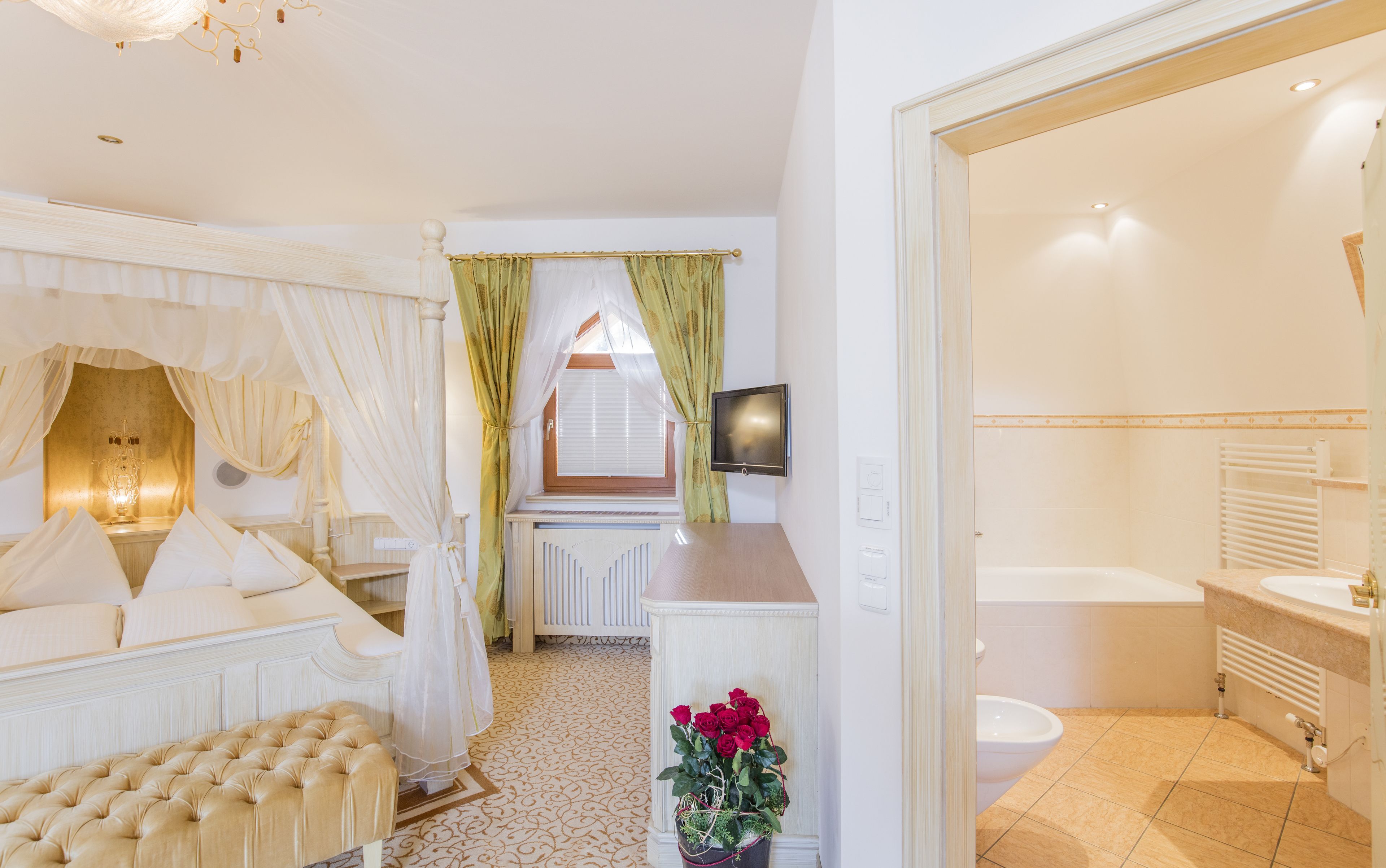 A bedroom with a canopy bed, a television, and a bathroom with a bathtub.