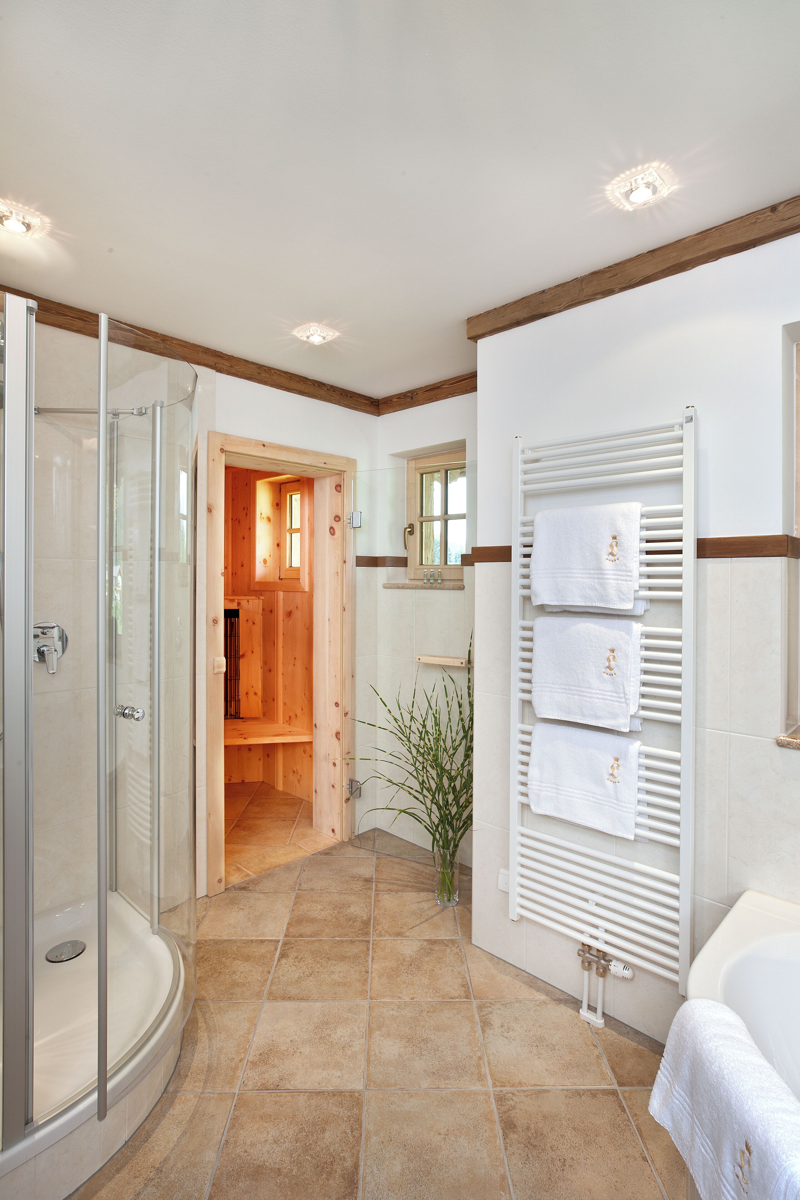 Un baño moderno con ducha de vidrio, puerta de madera y un perchero con varias toallas.