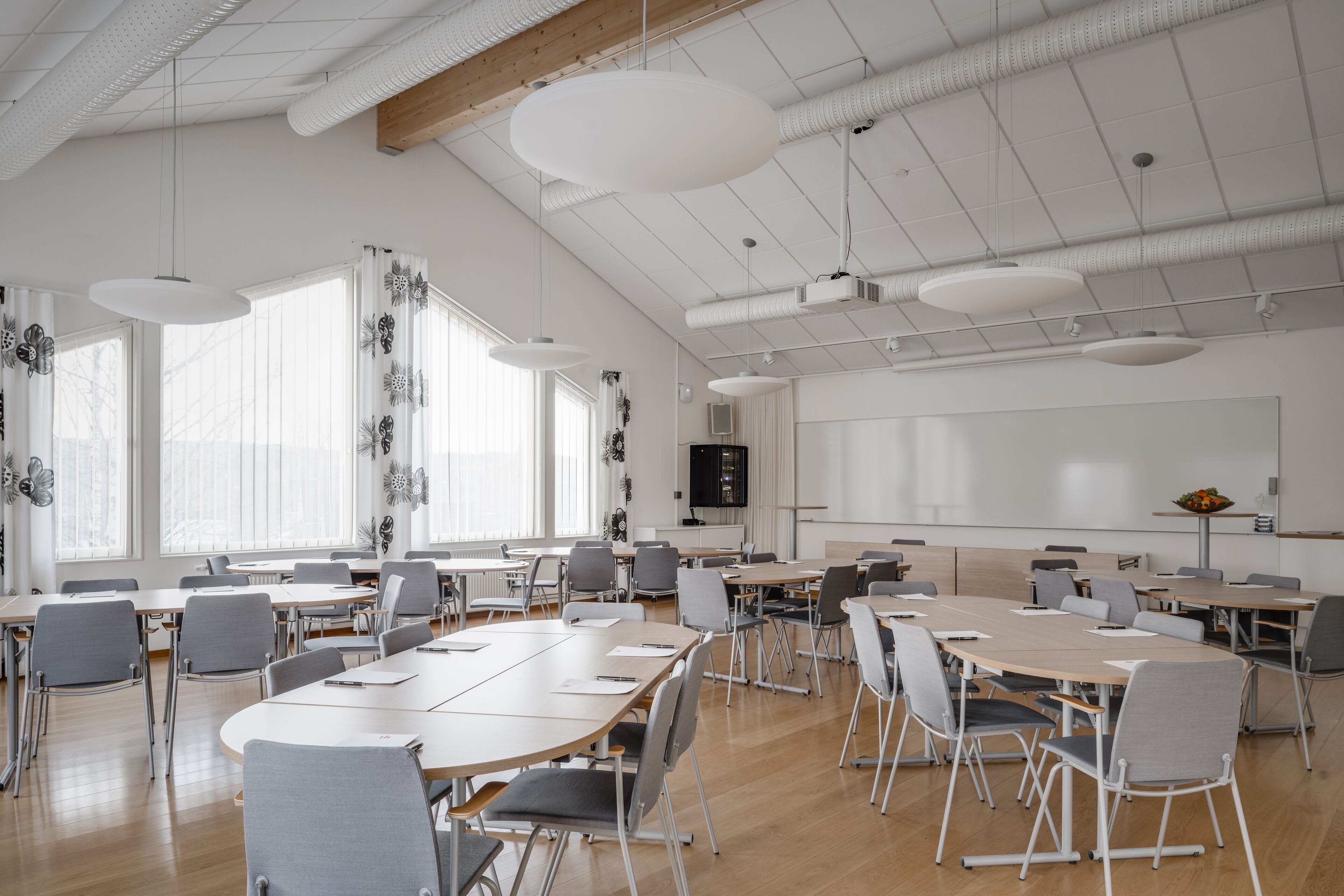 A spacious conference room with large tables and chairs, white walls, and a high ceiling with exposed beams.