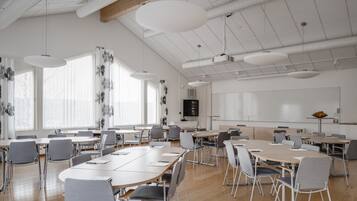 A spacious conference room with large tables and chairs, white walls, and a high ceiling with exposed beams.