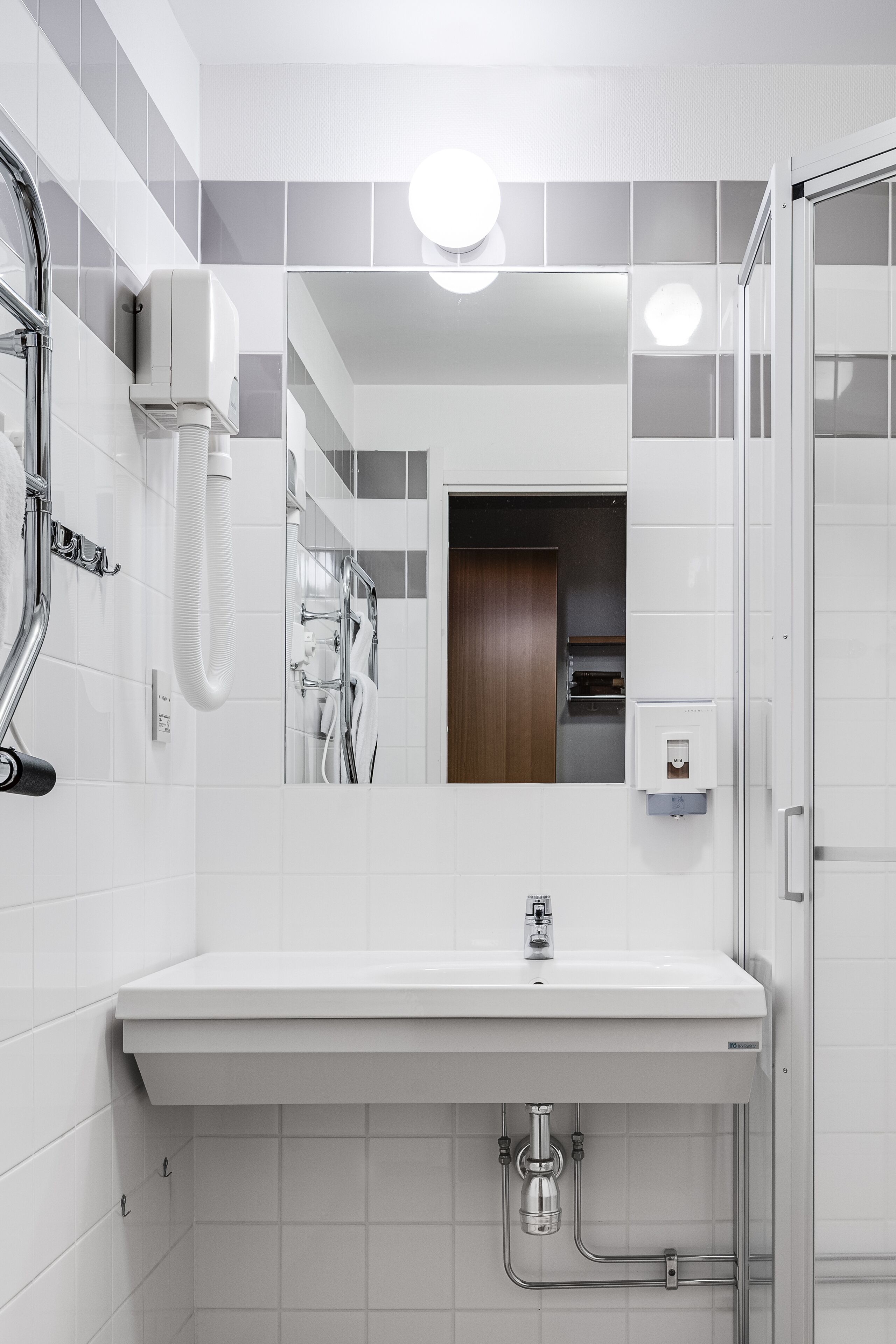A modern bathroom with a white sink, a mirror, and a shower area.