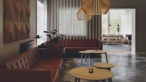Un salon moderne avec un canapé en cuir, deux petites tables rondes en bois et une grande fenêtre ornée de rideaux légers.