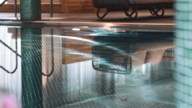 Une piscine intérieure avec un canapé en osier et un banc en bois en arrière-plan.