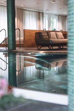 Une piscine intérieure avec un canapé en osier et un banc en bois en arrière-plan.