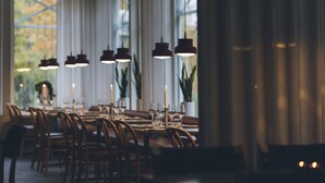 Un espace repas avec une longue table, des chaises, des lampes suspendues, des bougies et des plantes en pot.