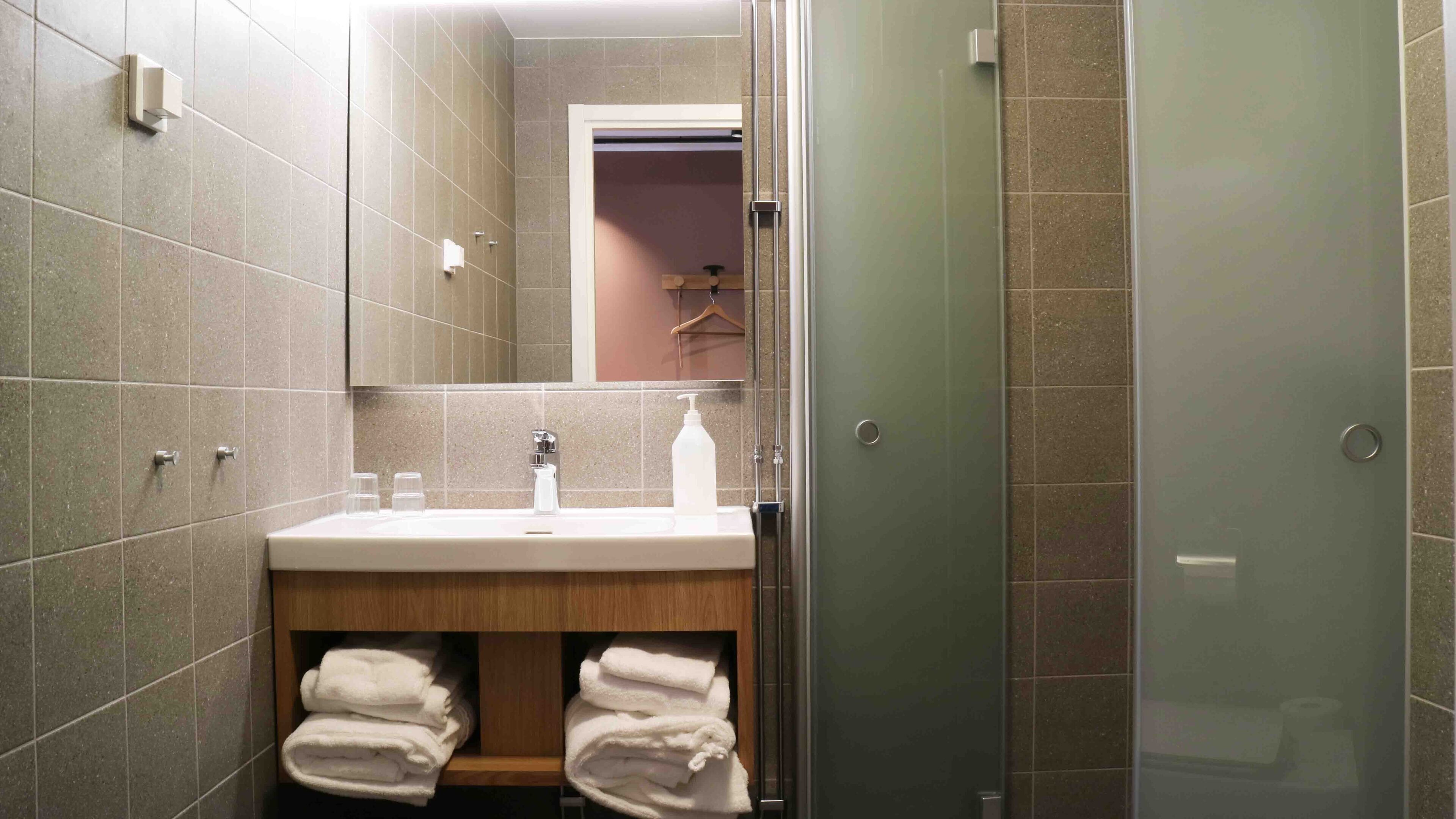 Un baño con lavamanos, espejo, toallero y zona de ducha.