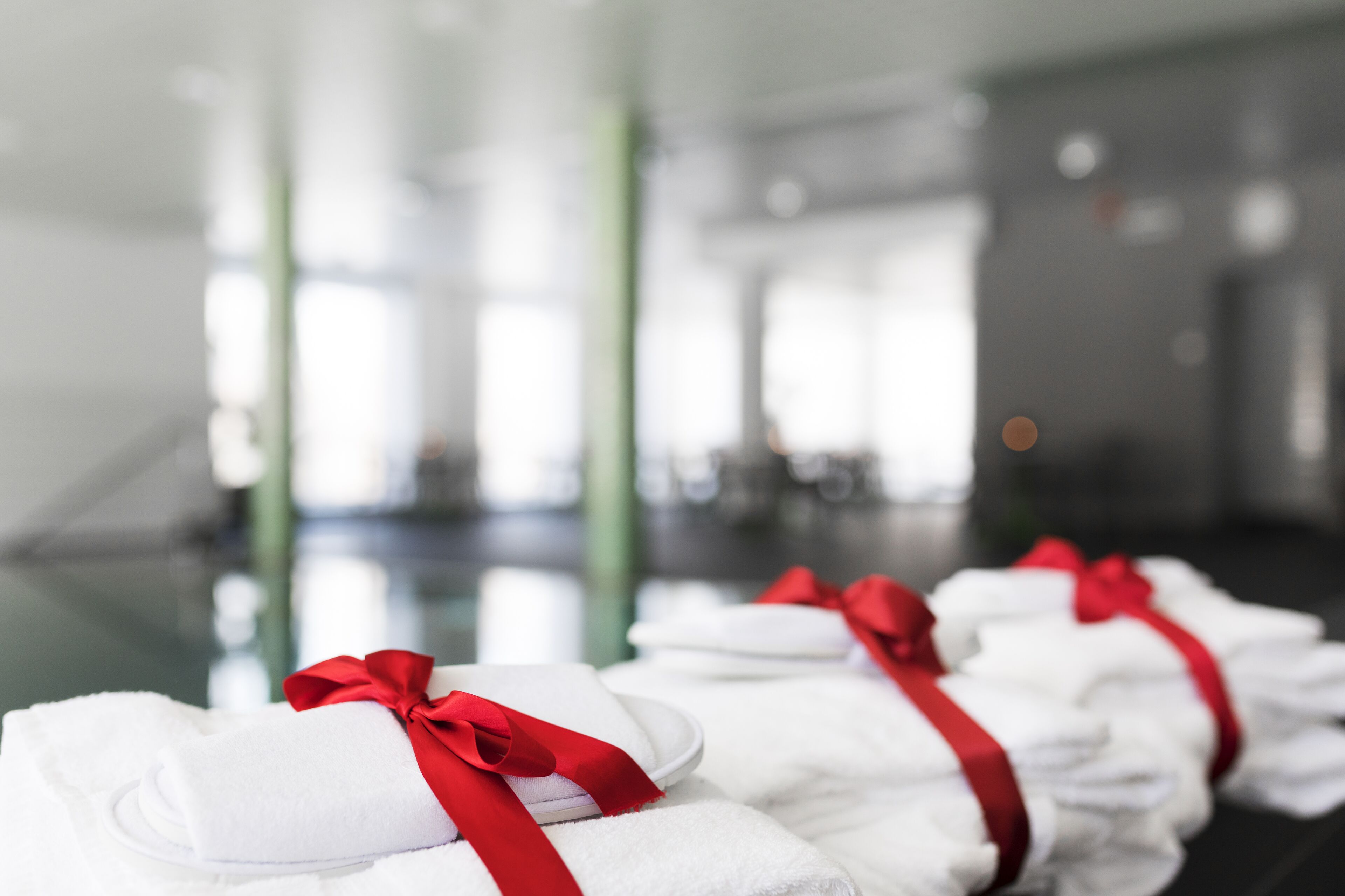 Neatly folded white towels with red ribbons, arranged in a row on a reflective surface in a well-lit indoor space.