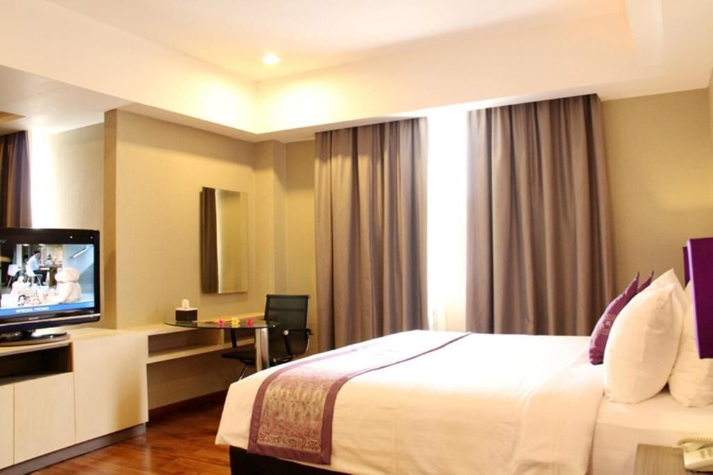 Habitació d'hotel amb llit, escriptori, cadira, televisió i cortines.