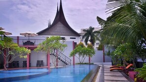 A swimming pool with a modern architectural building in the background, surrounded by palm trees and outdoor seating. - Truntum Padang (Padang)