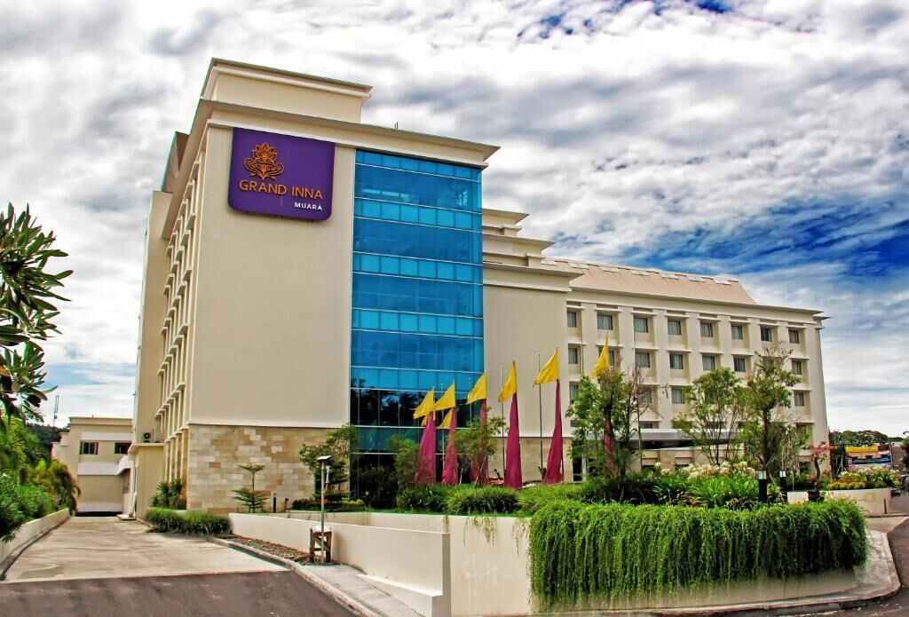 Imponente edificio del Grand Inn, con llamativa fachada de vidrio azul, exterior color beige y múltiples banderas amarillas.