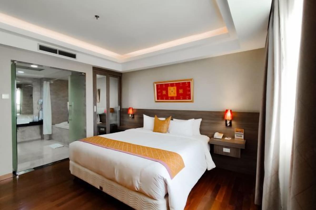 Una habitación de hotel con una cama grande, mesitas de noche, un espejo y una lámpara de pared.