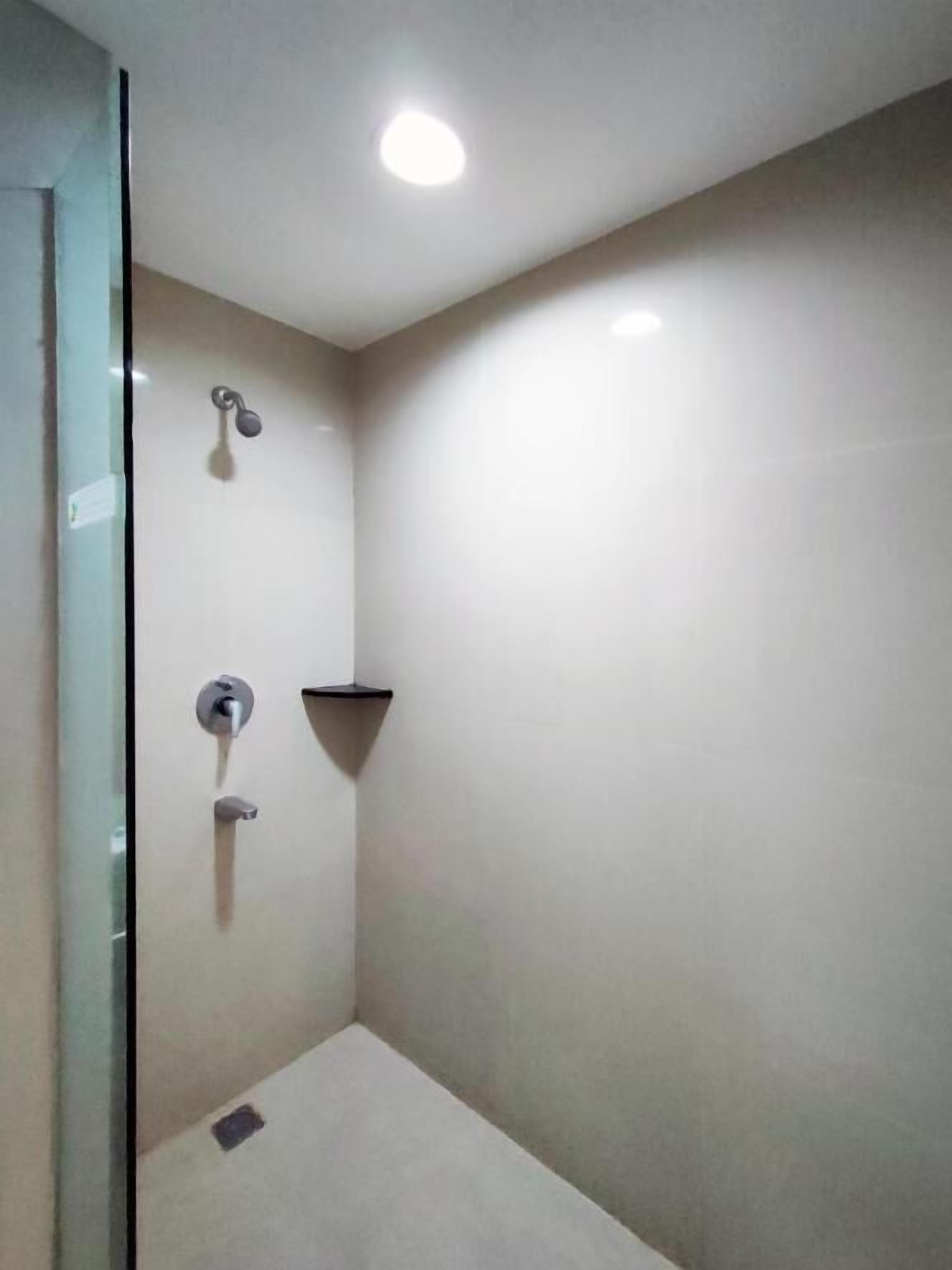 A small, modern shower area with a glass door, a wall-mounted showerhead, and a single light fixture on the ceiling.