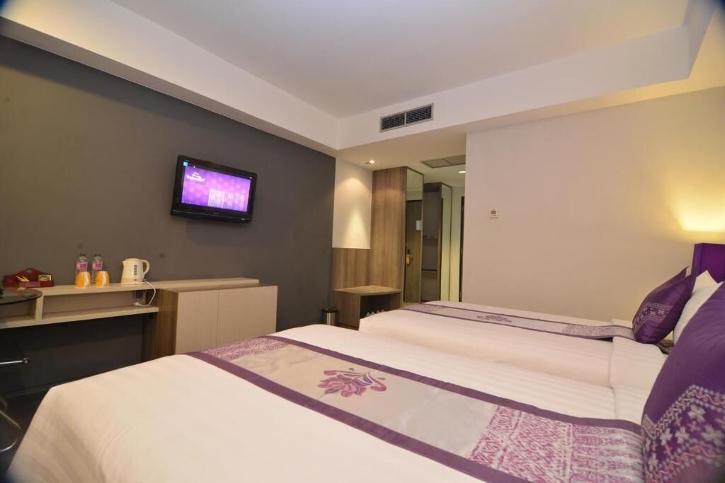 Habitación de hotel con dos camas, un televisor en la pared, un escritorio con lámpara y un espejo.