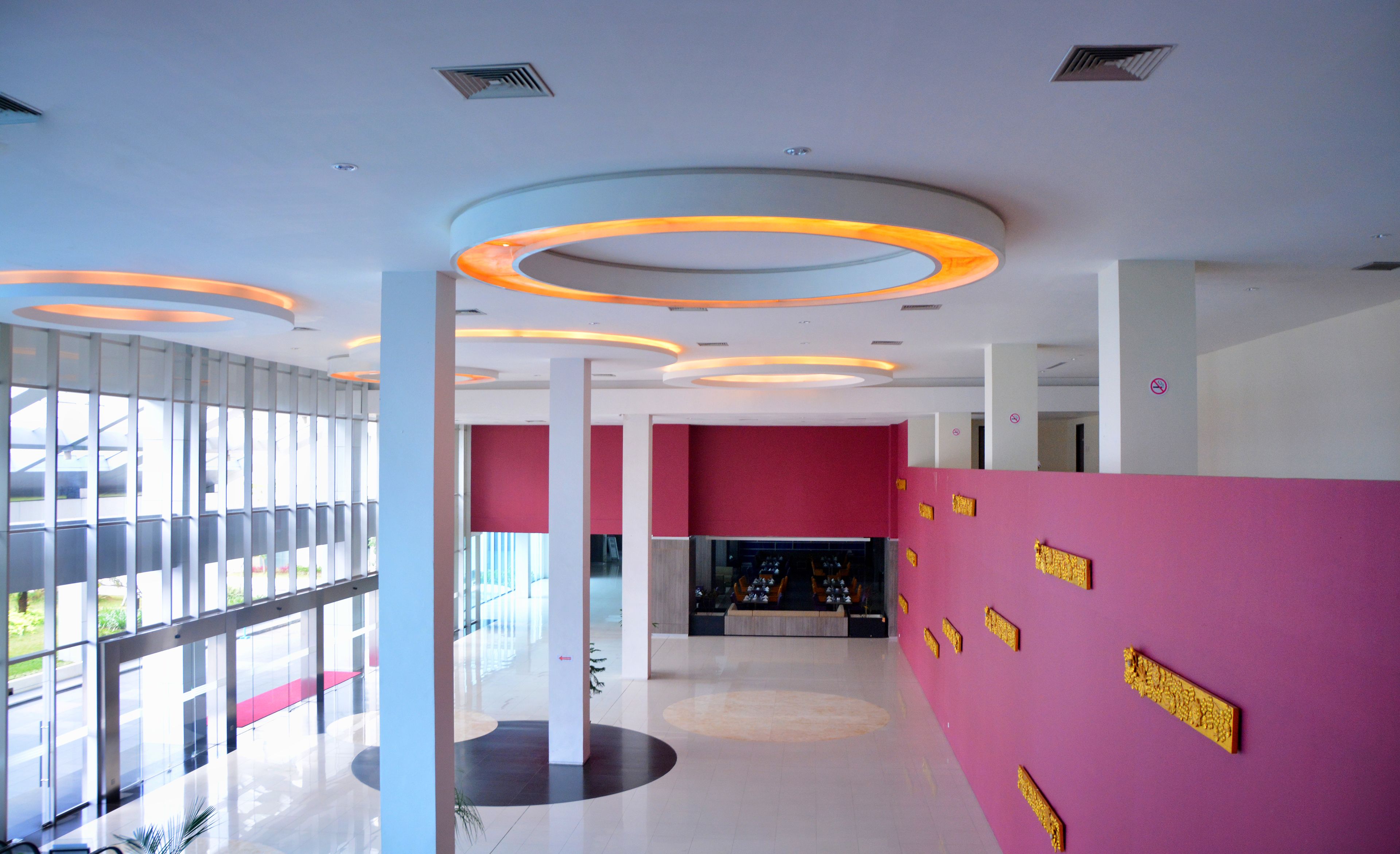 A modern lobby with a curved ceiling, large windows, and a pink wall with gold accents.