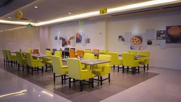 A modern dining area with yellow chairs and tables, a clean tiled floor, and wall art including a coffee cup.