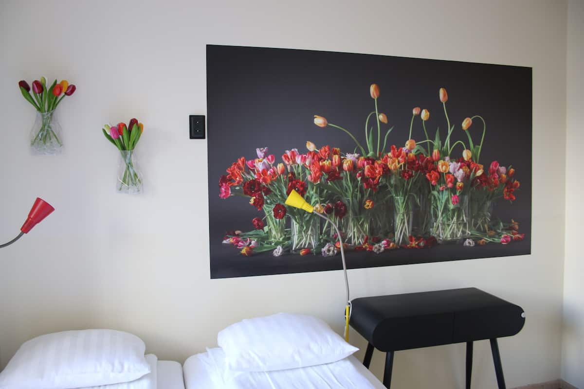 A hotel room with a large floral painting on the wall, a bedside table, and two white pillows.