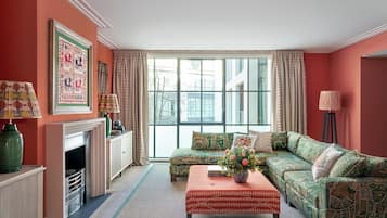 A living room with a fireplace, a sofa set, a coffee table with a vase, and a large window with curtains.