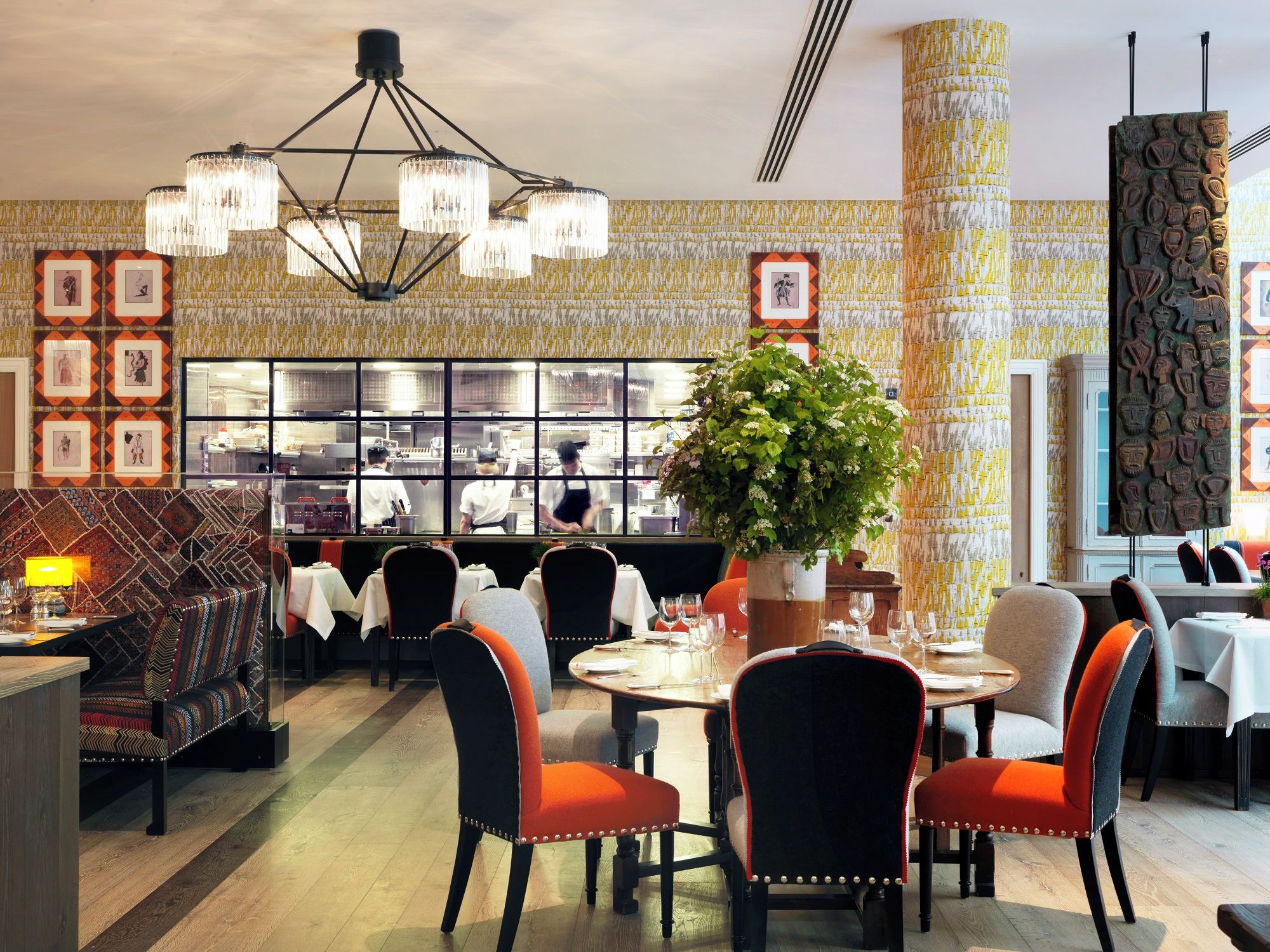 En restaurang med en central matsal, ett kök som syns genom ett stort fönster och väggar med ett mönster.