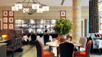 En restaurang med en central matsal, ett kök som syns genom ett stort fönster och väggar med ett mönster.