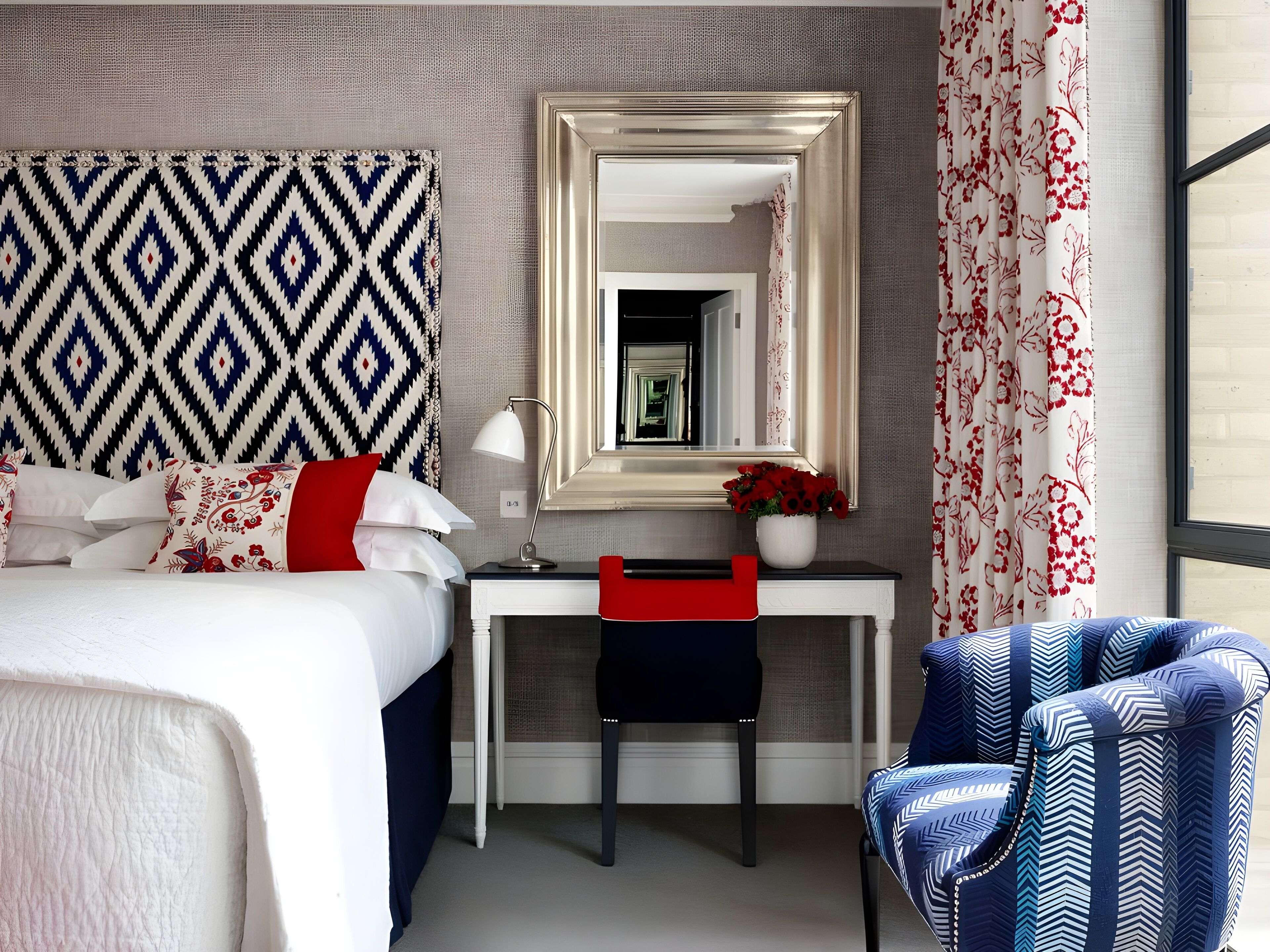 A hotel room with a bed, a desk, a chair, a mirror, and a window with curtains.