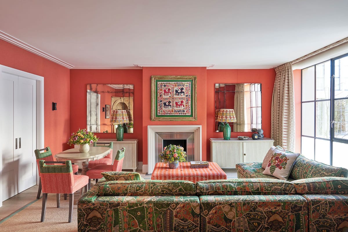A room with a red wall, a fireplace, a dining table with chairs, and a sofa.