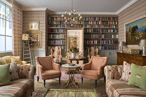A library room with two armchairs, a round table, and a bookshelf filled with books. - Ham Yard Hotel, Firmdale Hotels (London)