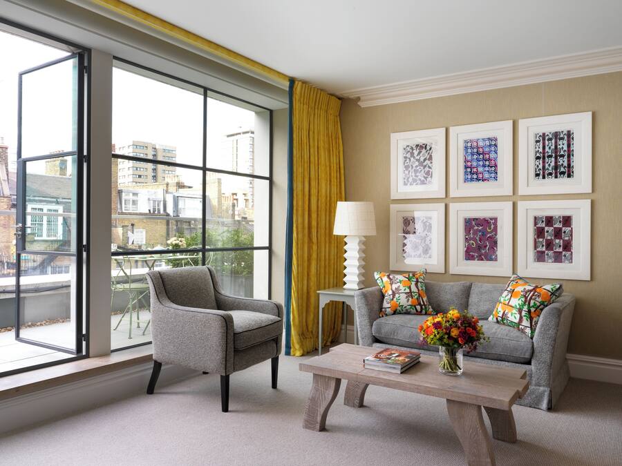 A modern living room with a grey sofa, a matching armchair, a wooden coffee table, and a large window with yellow curtains.