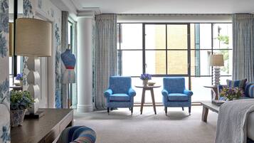 A hotel room with a large window, two armchairs, a small table, and a bed.