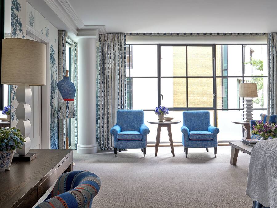 A hotel room with a large window, two armchairs, a small table, and a bed.