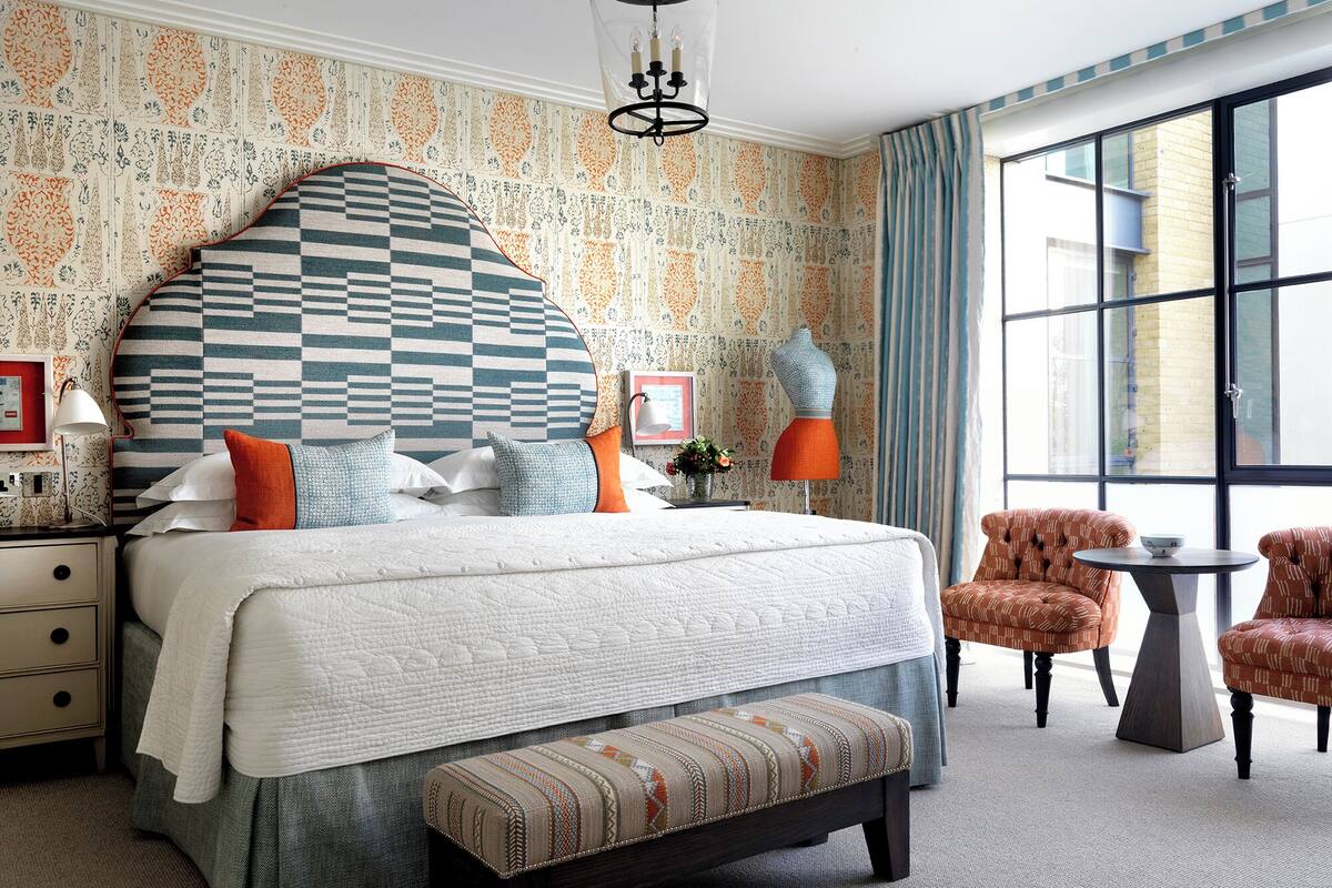 A neatly arranged bedroom with a large bed, a bench, two chairs, a small table, and a large window.
