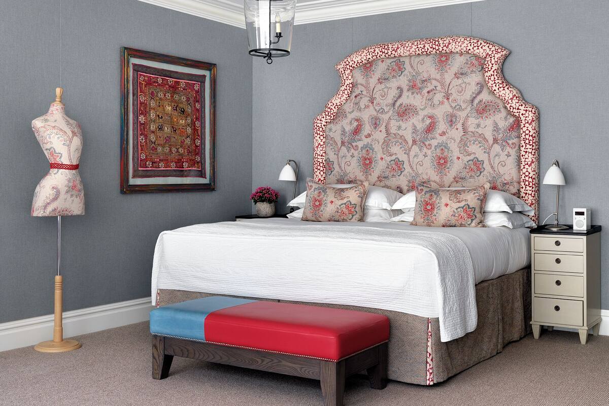 A bedroom with a large bed, a dresser, a nightstand, a lamp, a mannequin, and a framed picture on the wall.