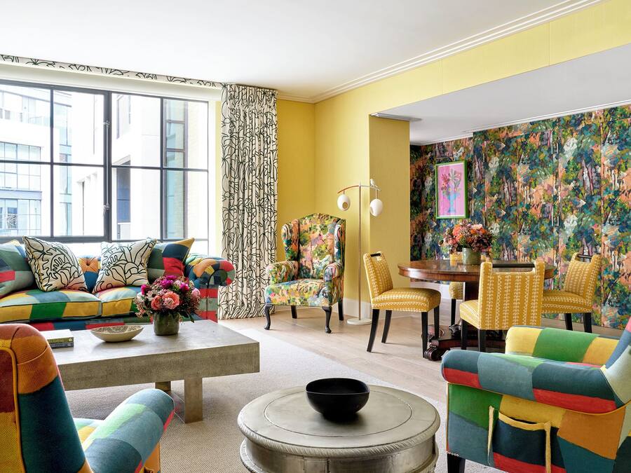 Un salon aux couleurs vives, doté d’une grande fenêtre, d’un canapé, de fauteuils et d’un coin repas.