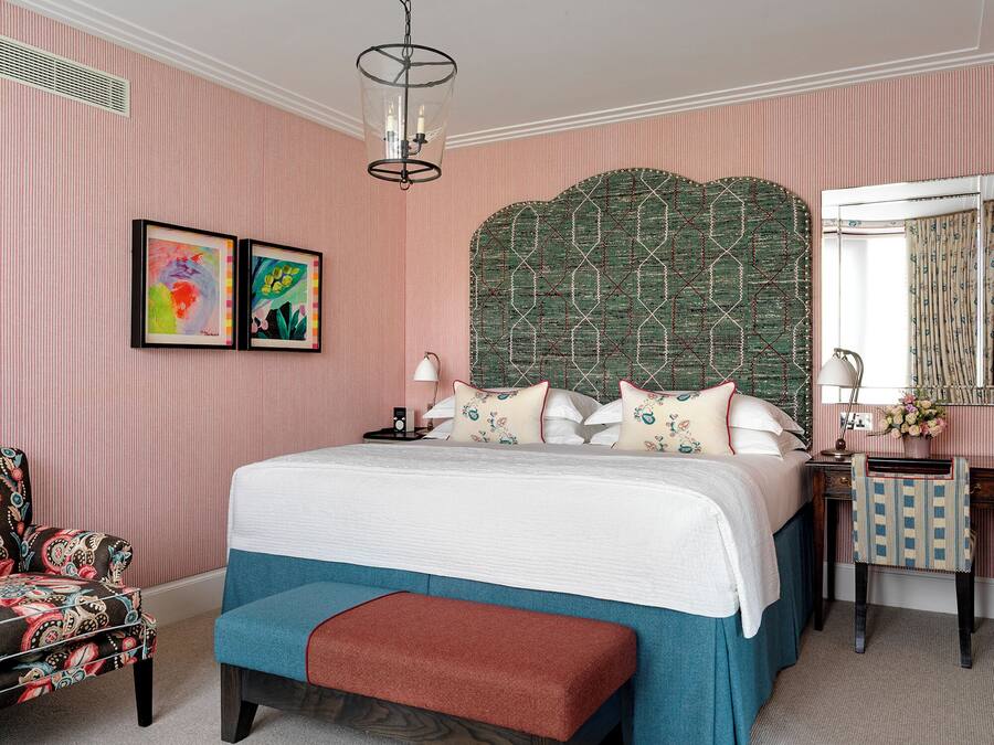 Quarto com uma cama grande, cabeceira com padrão geométrico, duas obras de arte emolduradas, mesa de cabeceira com luminária e uma cadeira com almofada estampada.