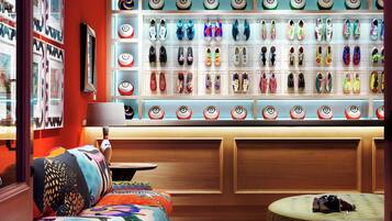 Una habitación con una pared llena de zapatos ordenados, un sofá colorido y un otoman redondo.