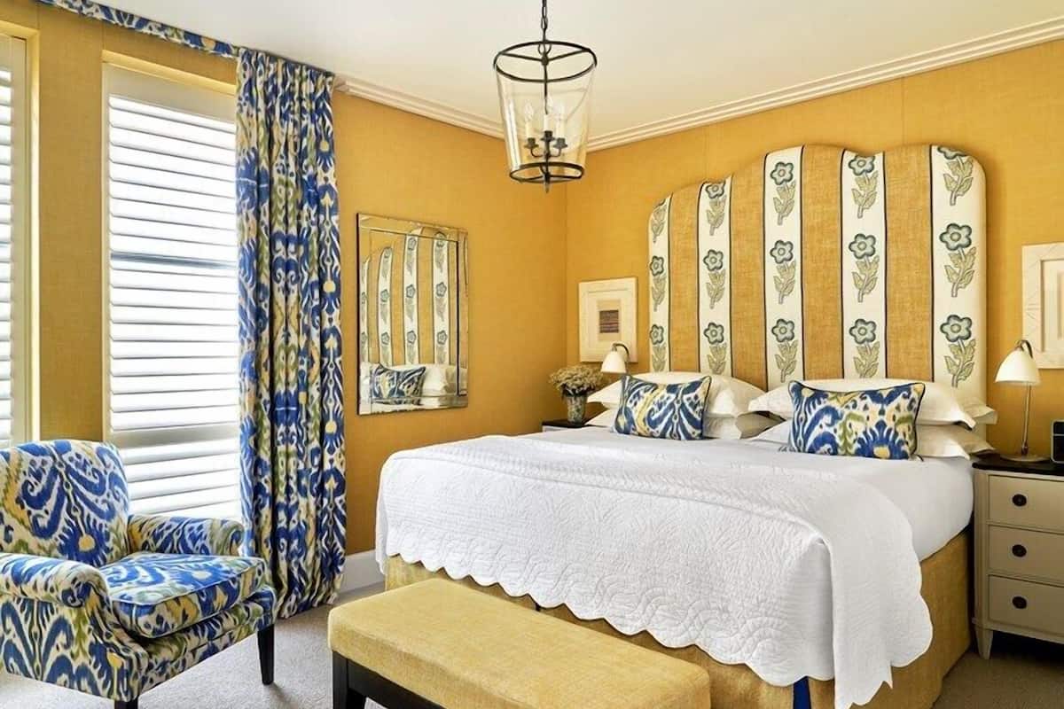 A bedroom with a large bed, a chair, a bedside table, and a window with curtains.