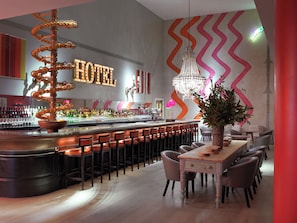 A hotel bar with a spiral light fixture, a chandelier, and a bar counter with stools. - Ham Yard Hotel, Firmdale Hotels (London)