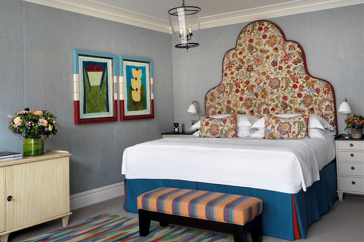A bedroom with a large bed, a bench, a dresser, a nightstand, a lamp, and two framed artworks on the wall.