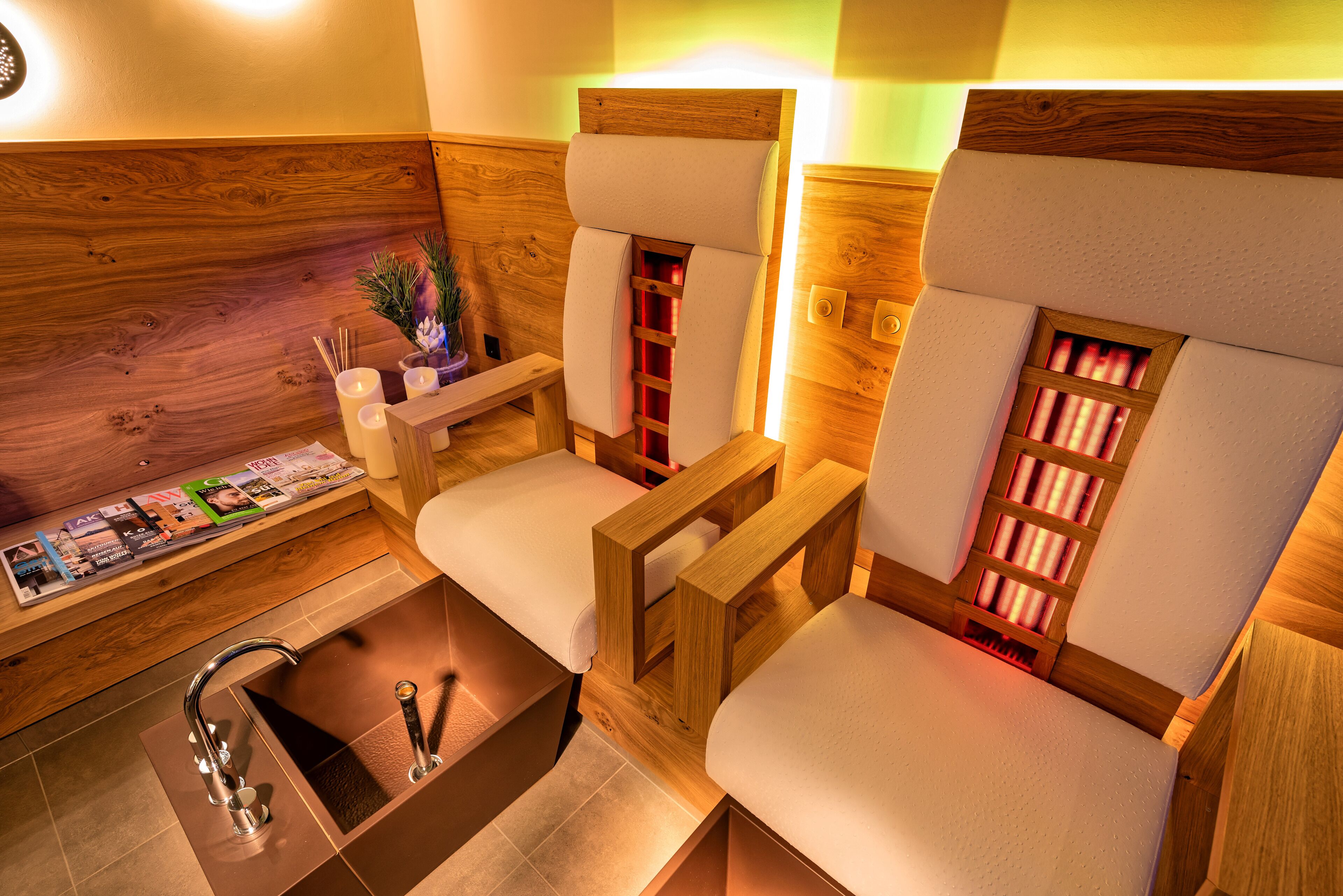 A spa room with wooden headrests, a wooden bench, a small table with magazines, and a sink with two faucets.