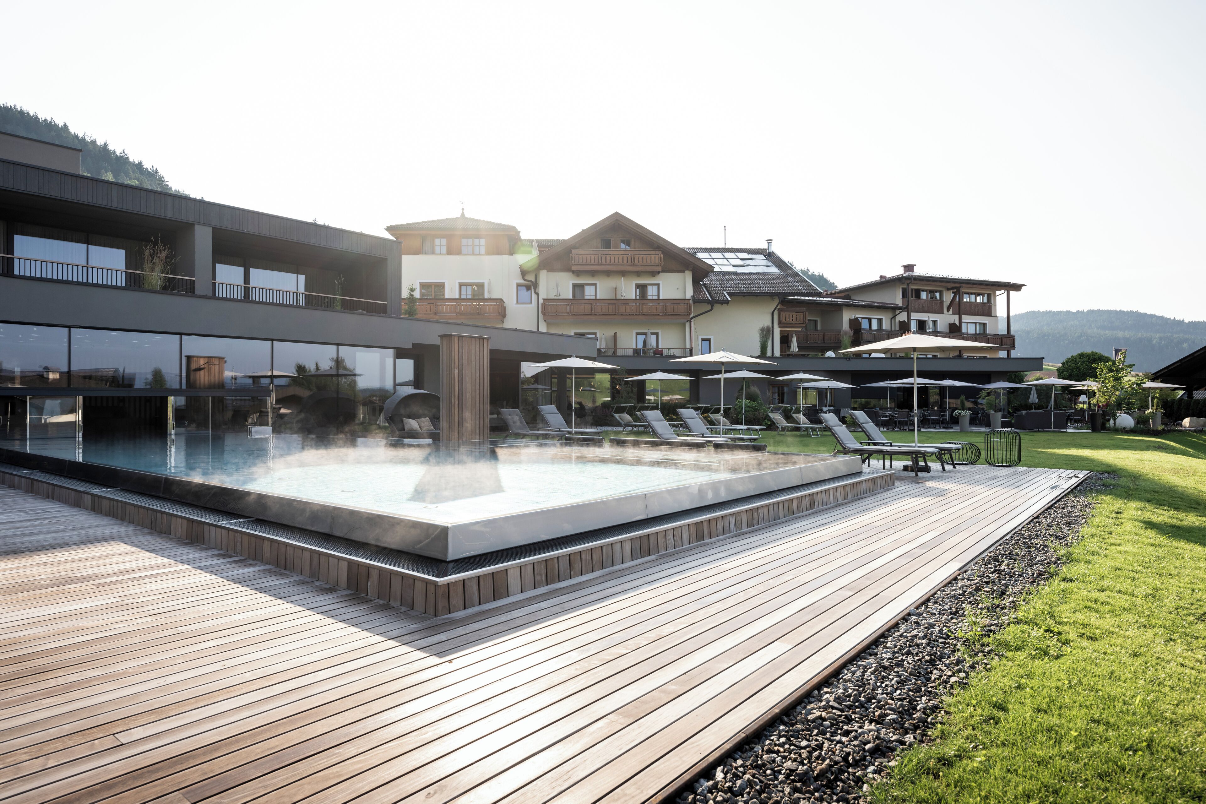 Un'area piscina moderna all'aperto con lettini, una vasca idromassaggio e un solarium in legno.