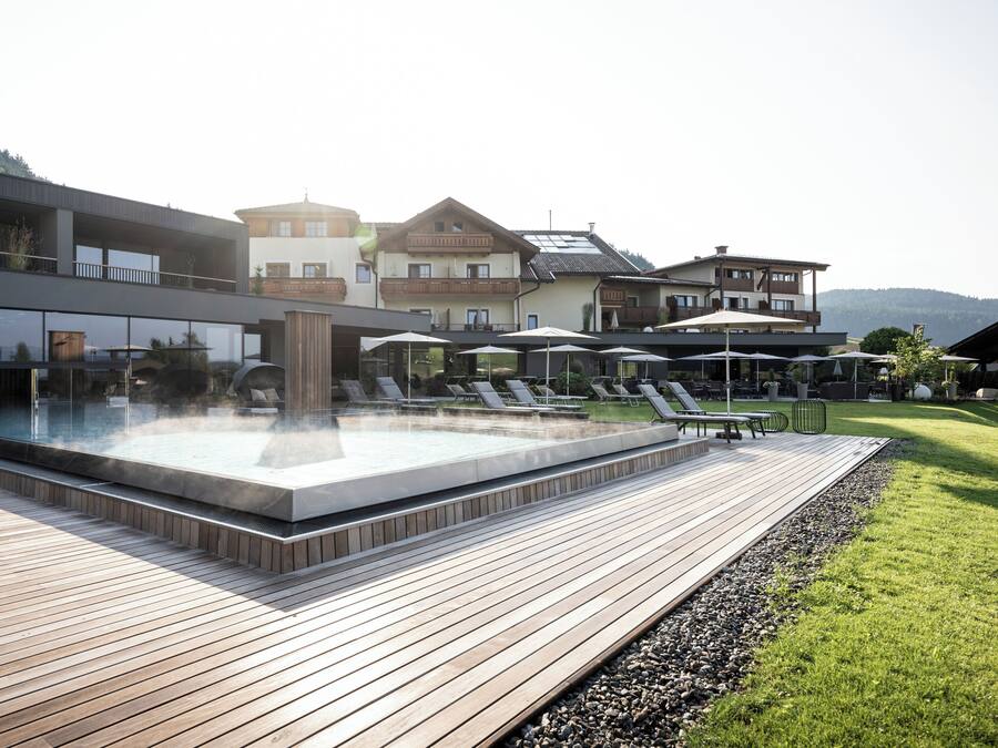 Un'area piscina moderna all'aperto con lettini, una vasca idromassaggio e un solarium in legno.