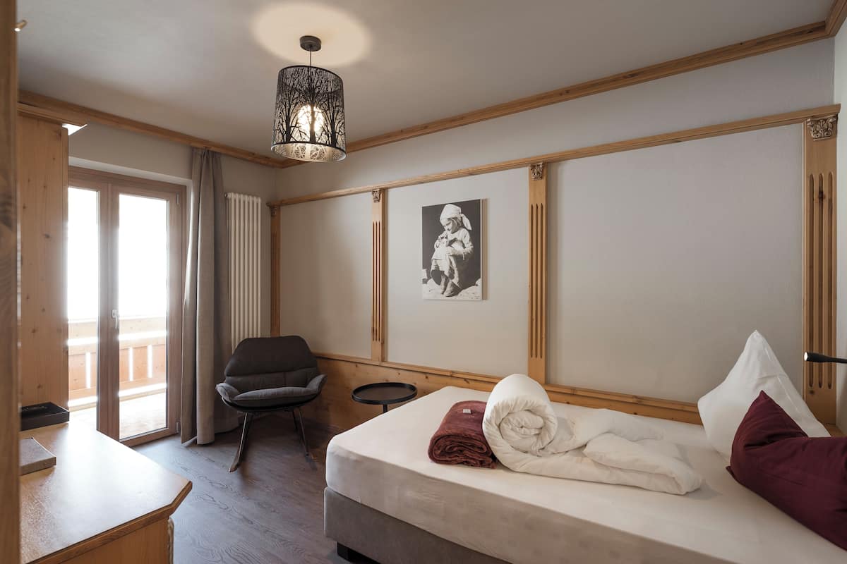 Hotellihuone, jossa on sänky, tuoli, pieni pöytä, taulu seinällä ja ikkuna, jossa on verhot.
