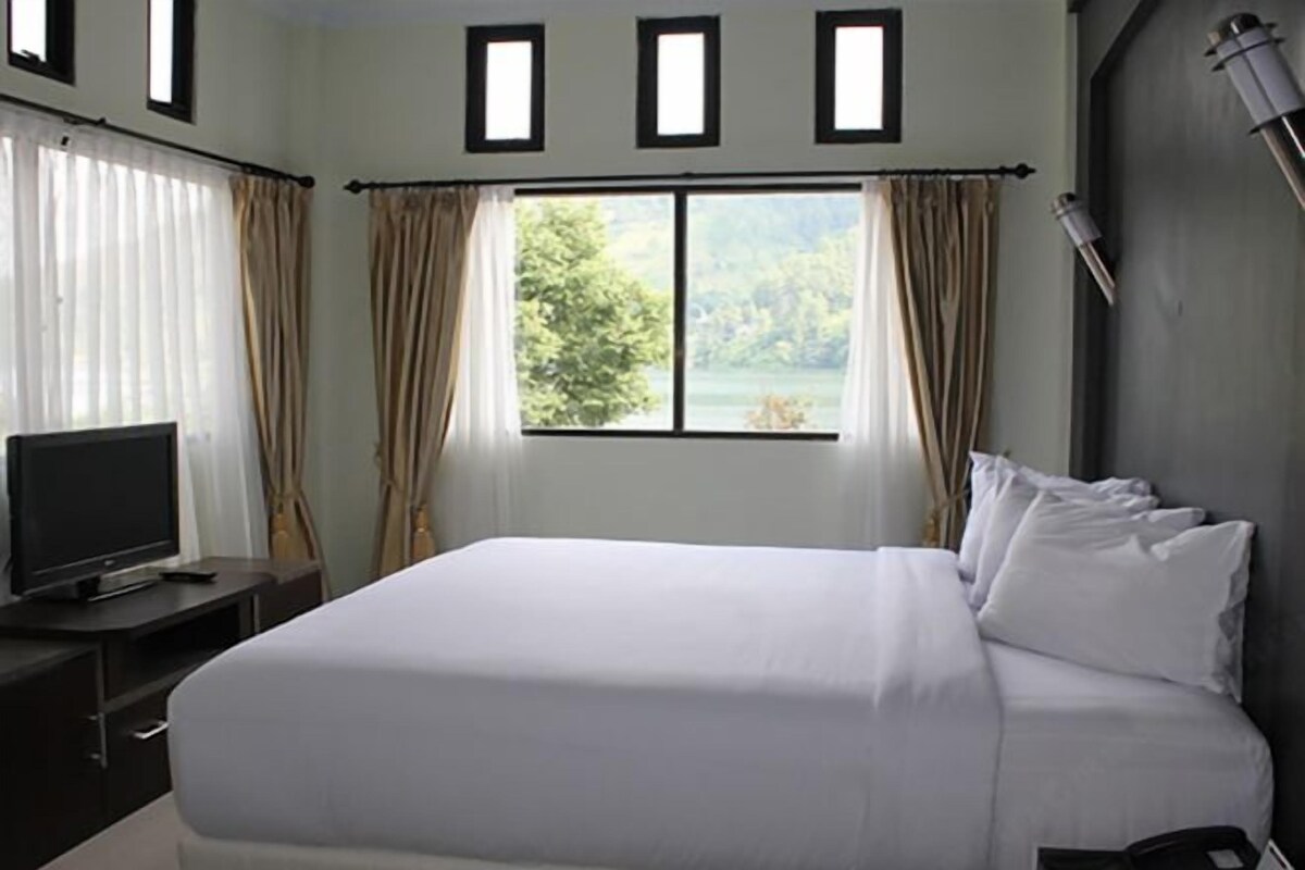 A hotel room with a large bed, a TV on a stand, and a window with curtains.