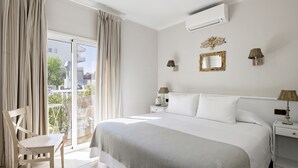 A bedroom with a large bed, a chair, a nightstand, and a wall-mounted lamp. - Hotel La Goleta (Llanca)