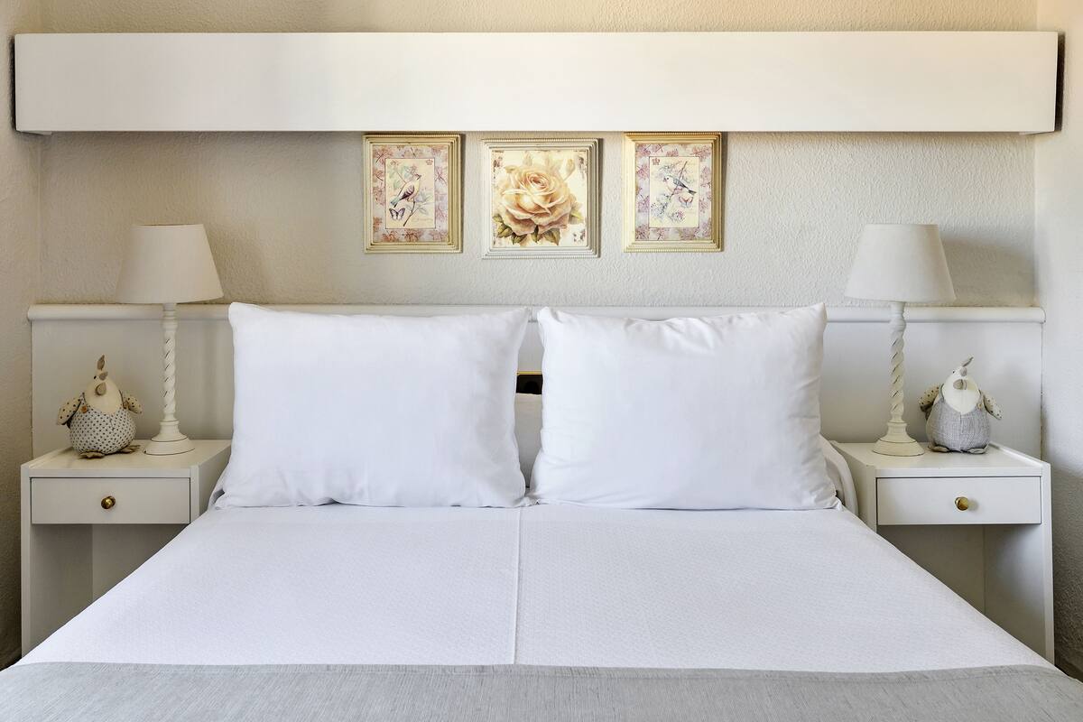 A neatly made bed with white linens, two bedside tables with lamps, and three framed pictures on the wall.