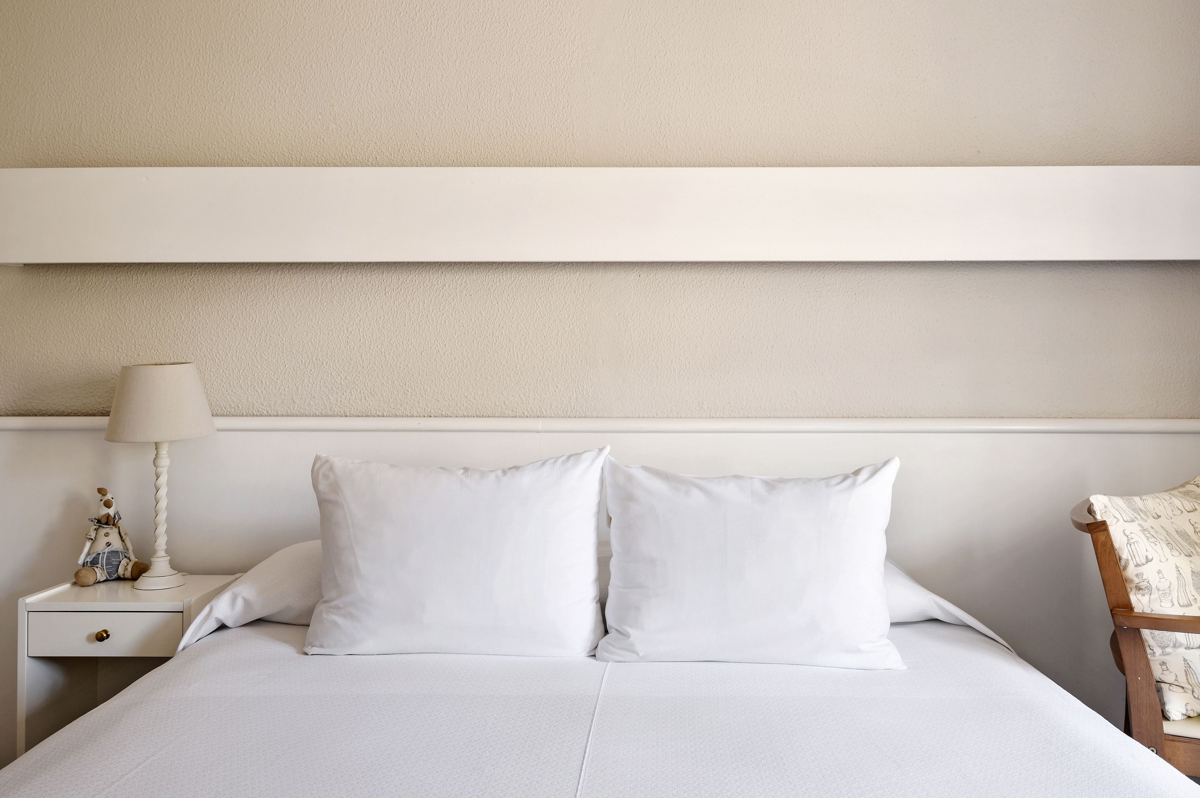 A neatly made bed with white linens, a bedside lamp, and a small decorative item on the nightstand.