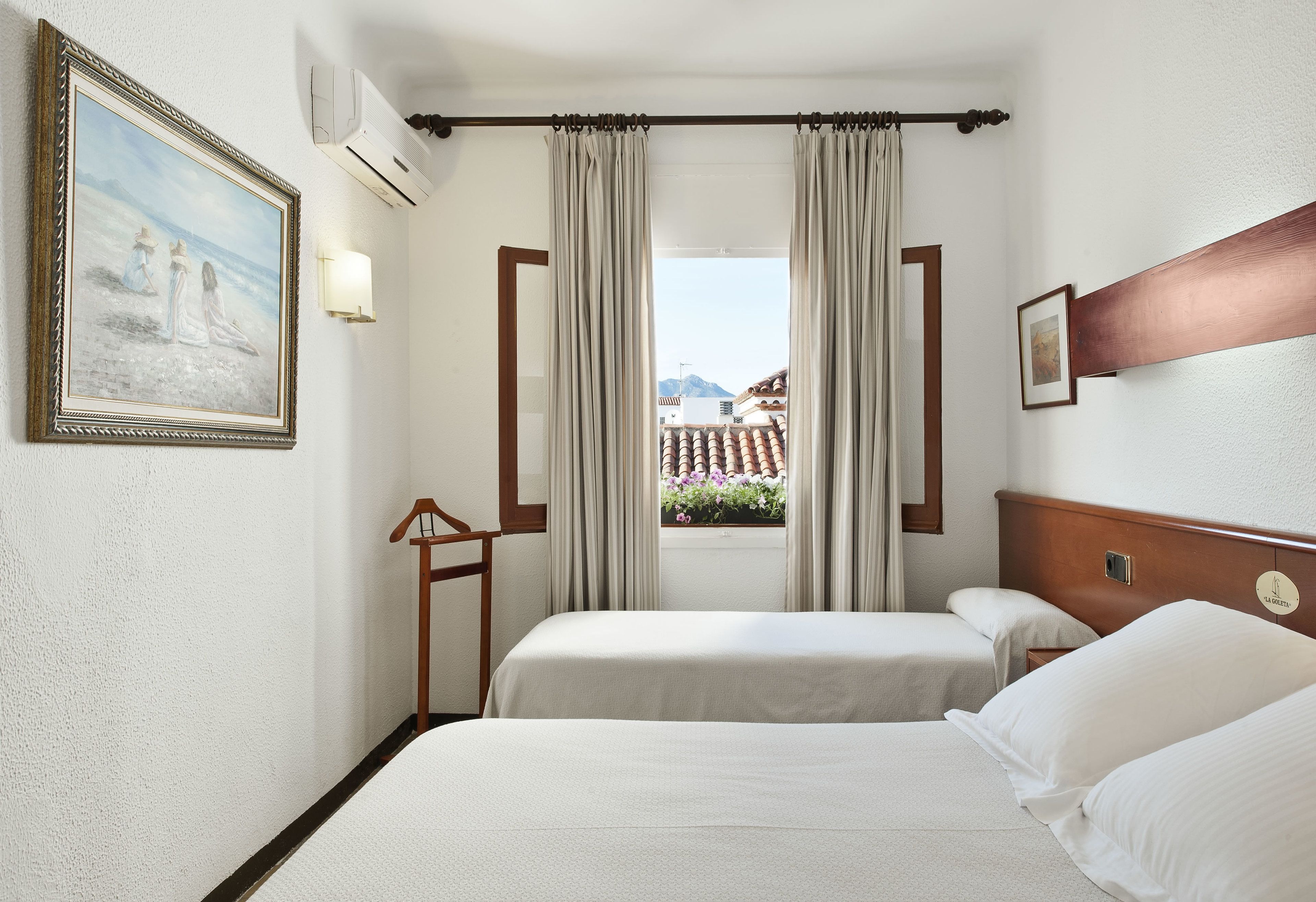 A hotel room with two beds, a window with curtains, a painting on the wall, and an air conditioning unit.