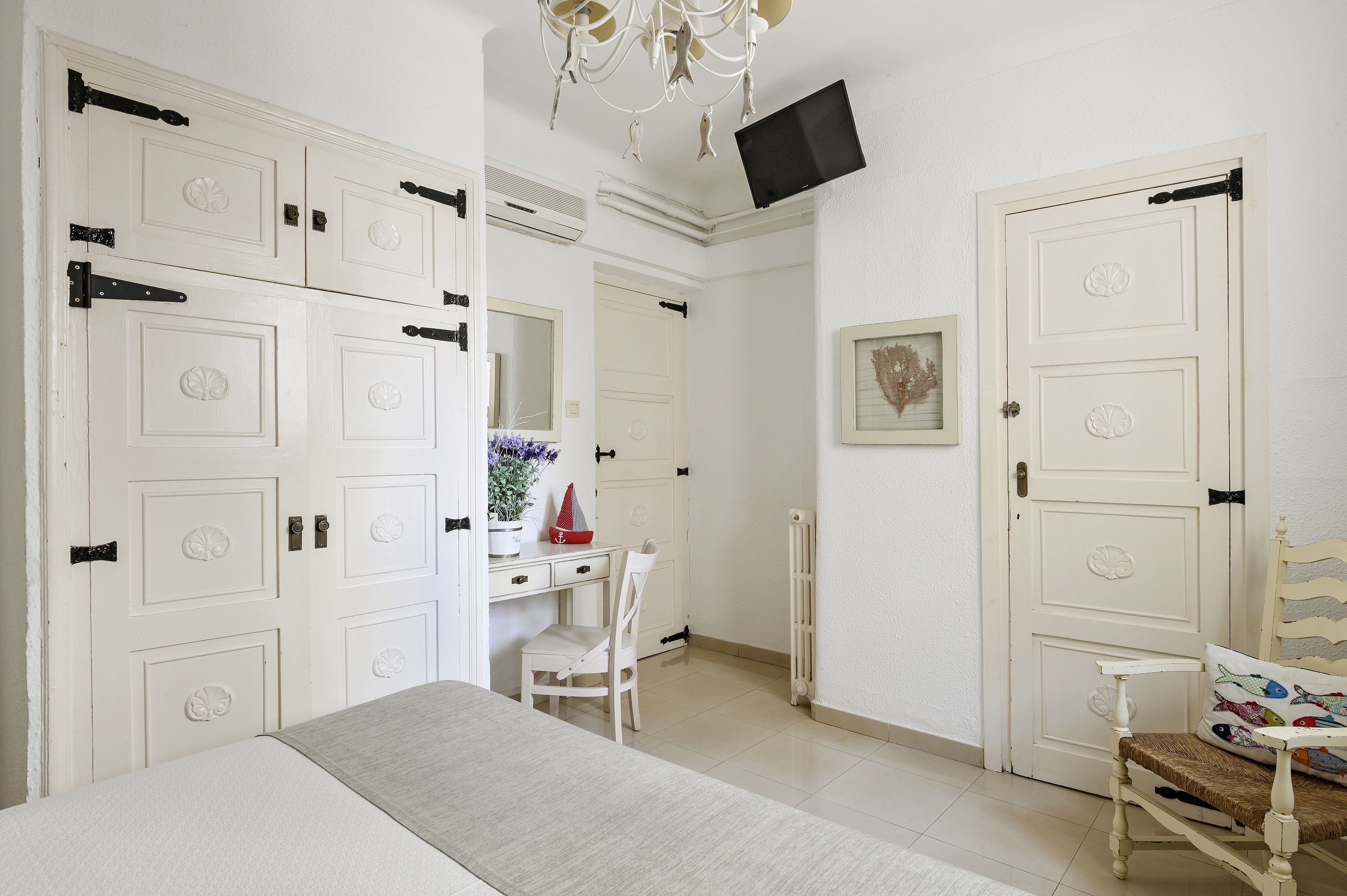 A bedroom with a bed, a desk with a chair, a TV mounted on the wall, and white doors with black handles.