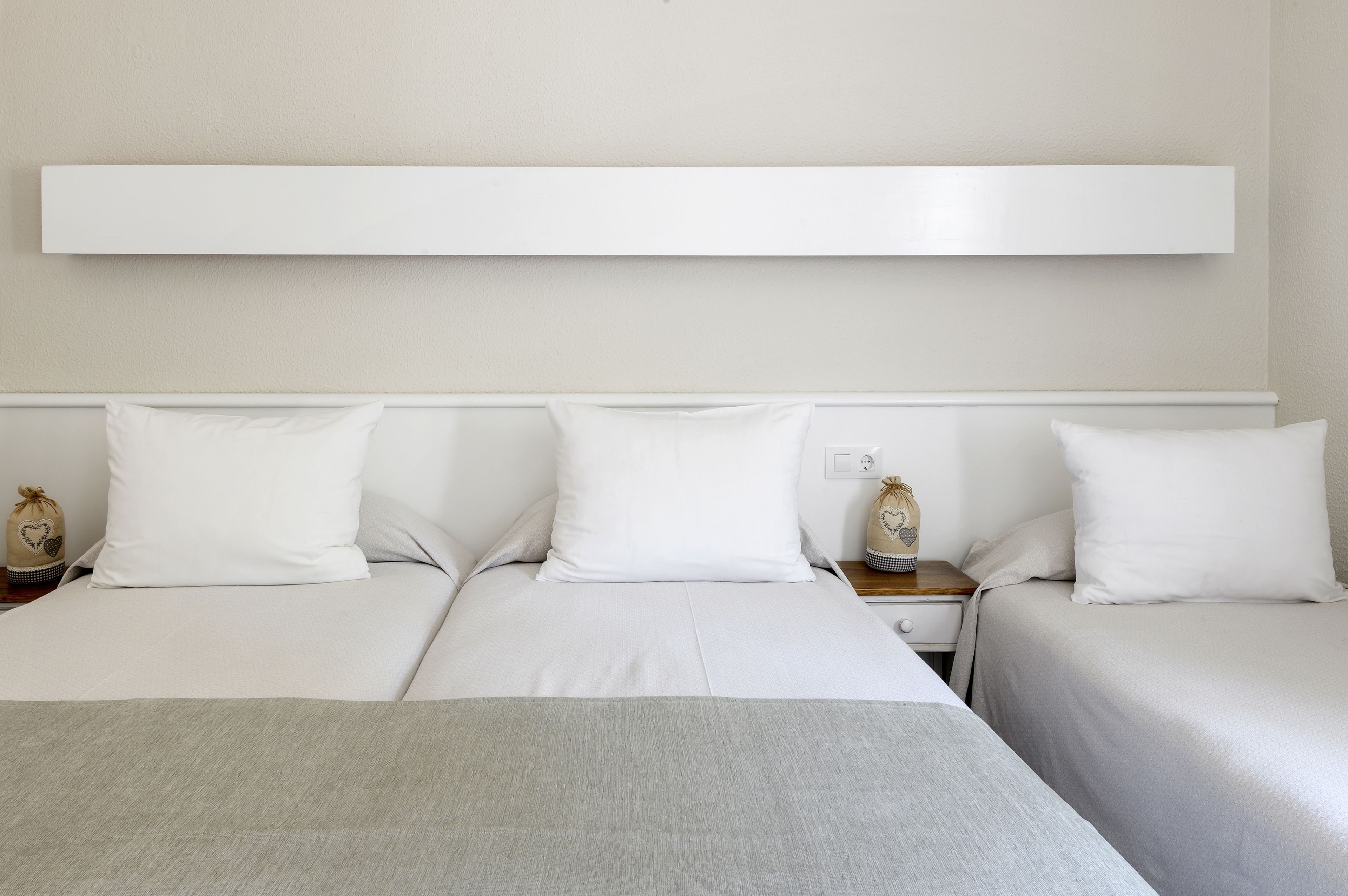Une chambre d’hôtel avec deux lits, du linge de lit blanc, un plaid gris et une table de chevet avec une lampe.