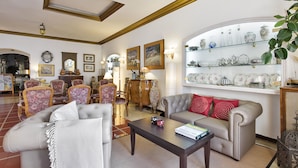 A living room with a sofa, armchairs, a coffee table, and a glass display cabinet with decorative items. - Hotel La Goleta (Llanca)